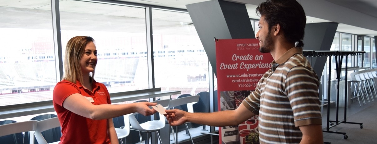 An event coordinator standing behind a table registers participants for an event and hands a man a nametag.