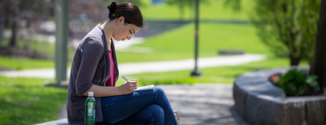 a student sitting outside and writing in a notebook 