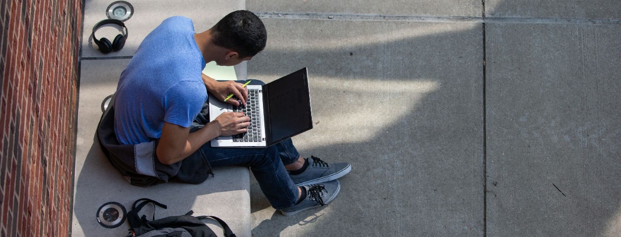 A student works on a laptop on UC's campus