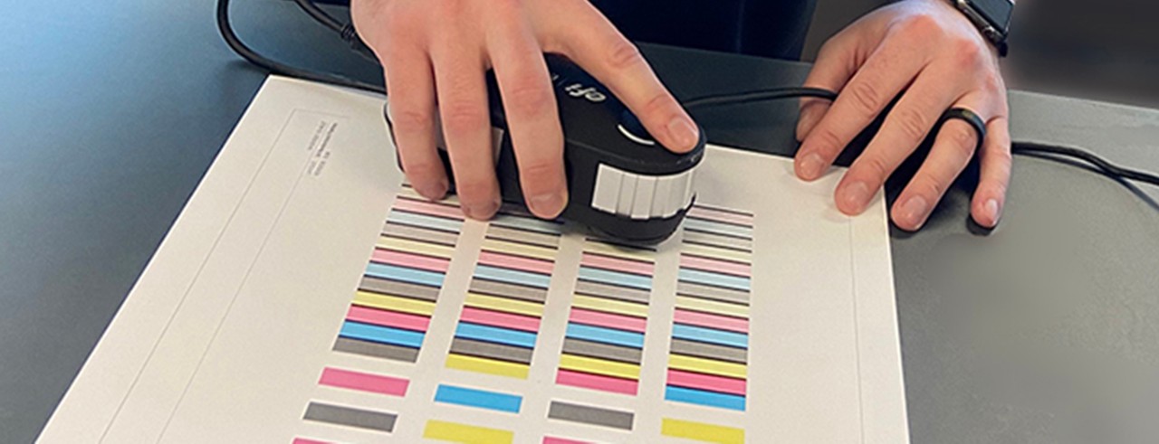 Hands using device to check color of printing