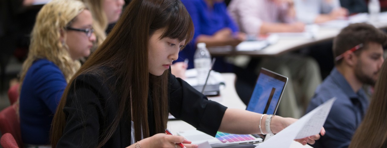 A Student works looks through notes in a notebok in a lecture hall