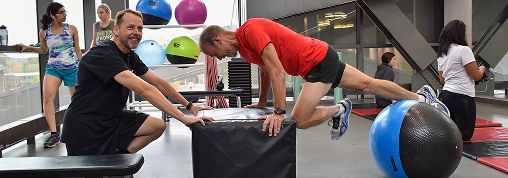 Trainer working with member at the Campus Recreation Center while other guests workout alone.