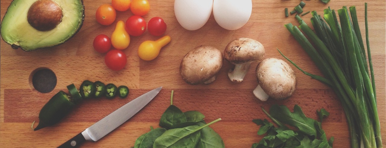 Vegetables, eggs and a knife laid out on a wood cutting board