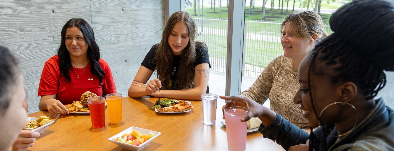 Students sit at a long rectangular table eating and chatting in a University of Cincinnati dining center.