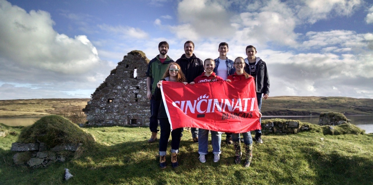 Honors students holding a UC banner in front of ancient ruins