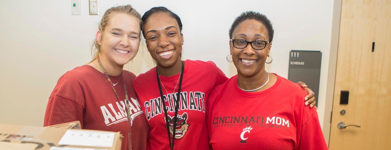 three females smile posing for a picture. One woman is wearing a shirt reading "Cincinnati Mom"