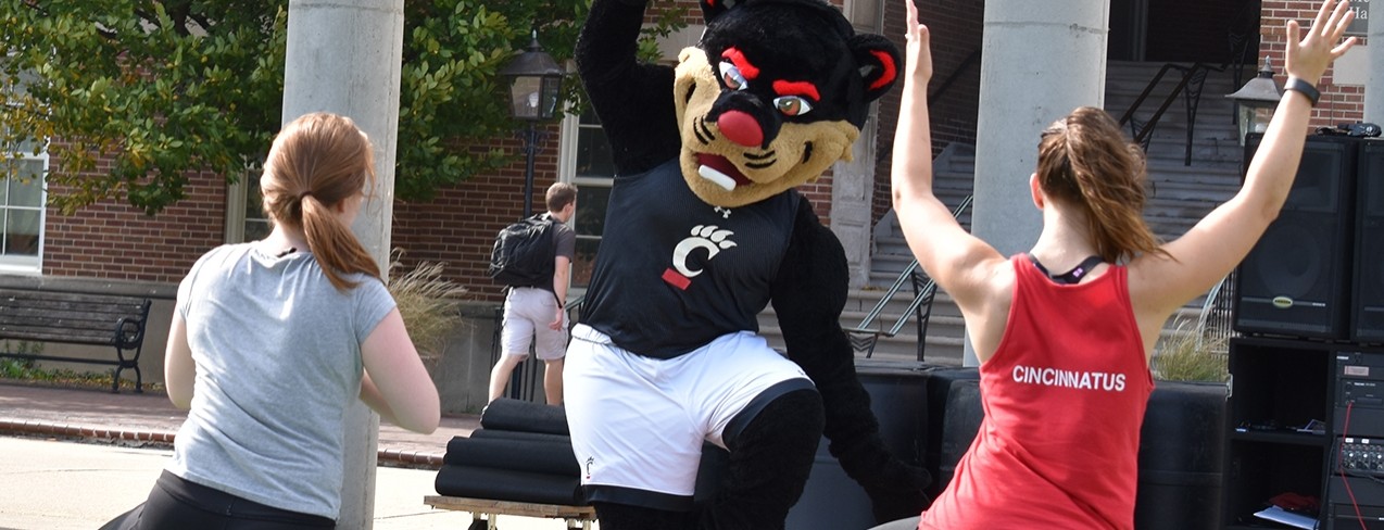 The Bearcat Mascot appears to be teaching a Campus Recreation yoga class outside. Two students are participating.