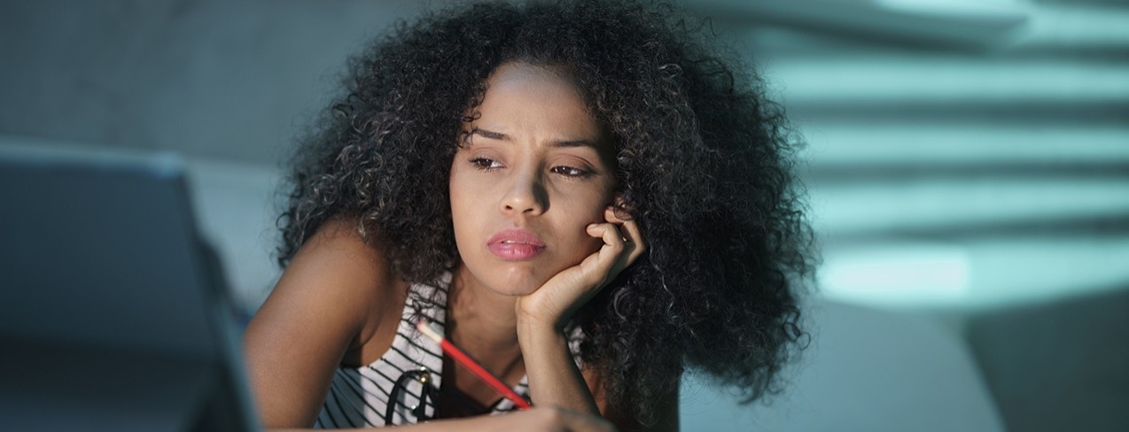 Female student laying on bed, concentrating on what is on her laptop.