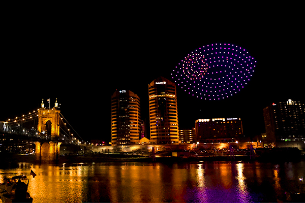 Image of the drones creating the Blink eye logo shape over the Cincinnati River with the Kentucky skyline and Roebling bridge in the background