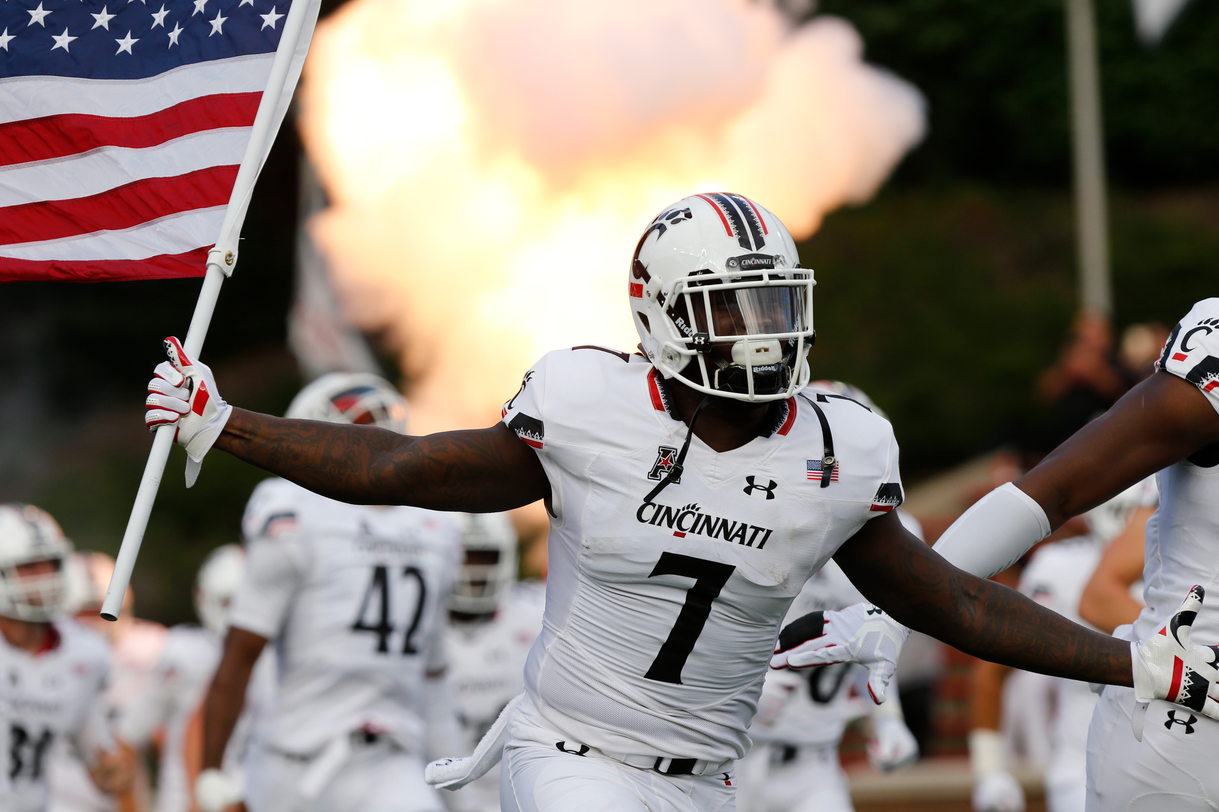 A UC football player takes the field while holding an American flag