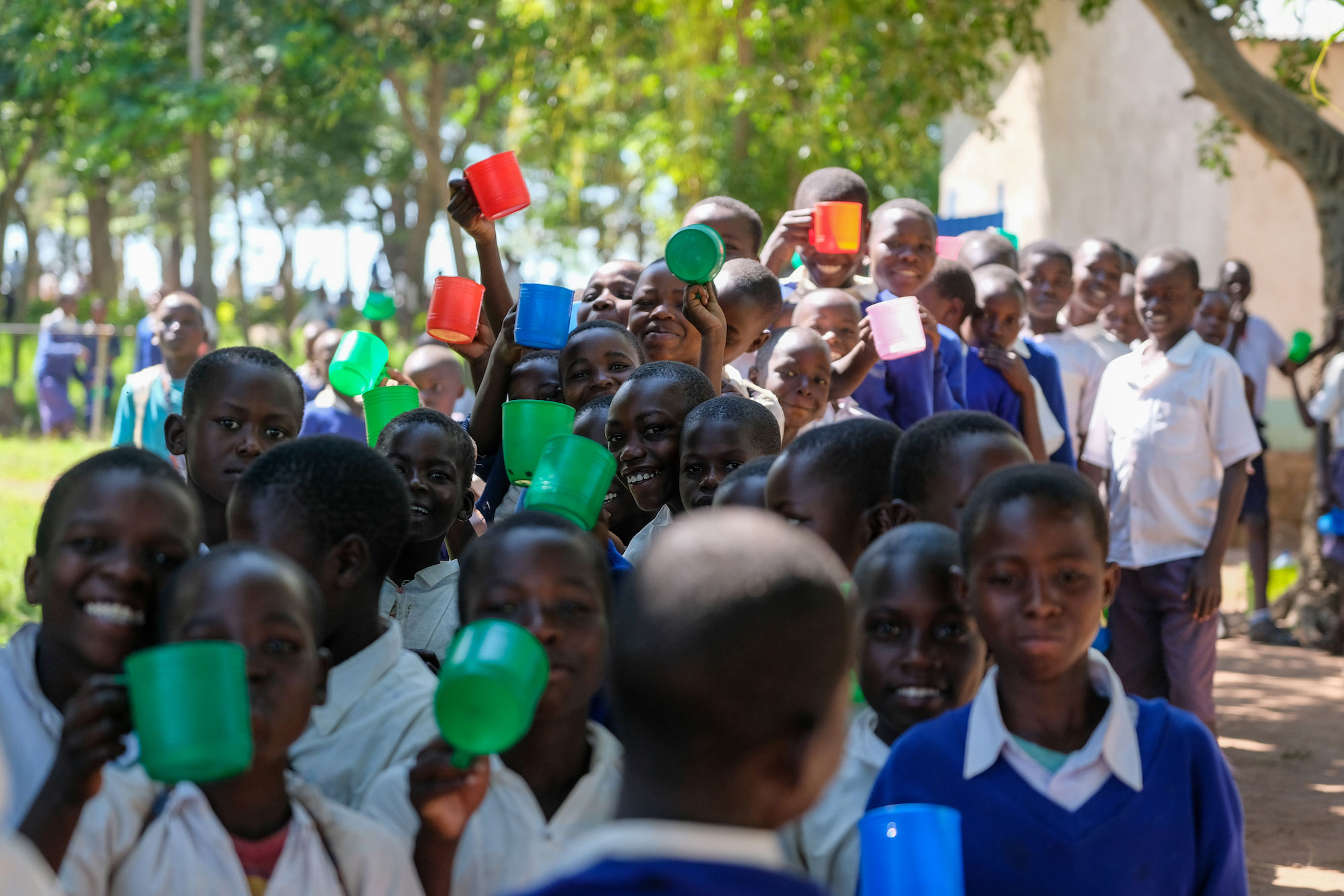 Dozens of Tanzanian school children line up with cups for porridge