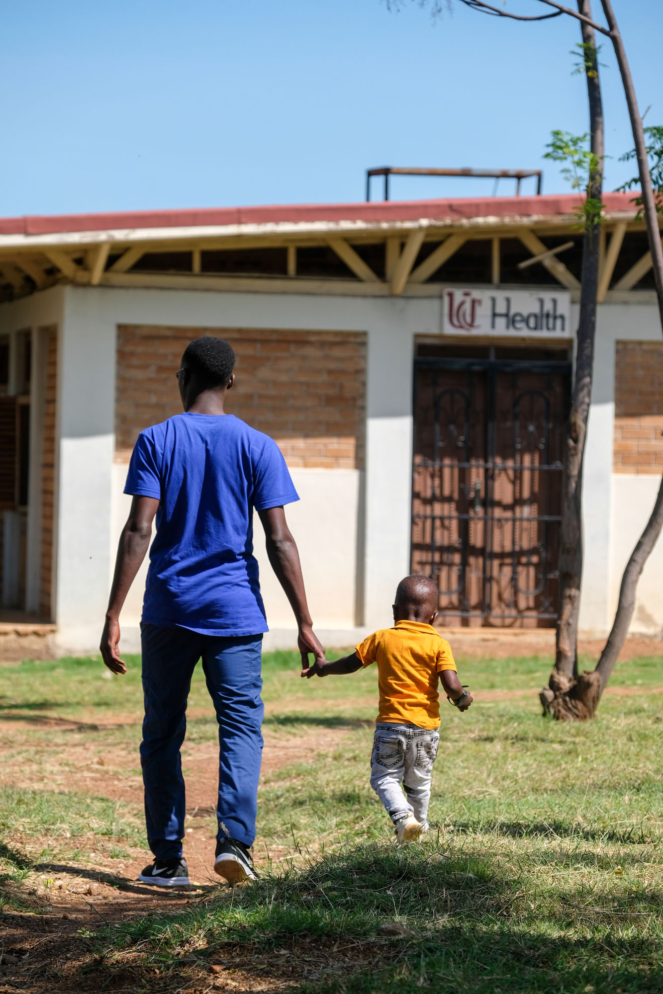 Man walks hand-in-hand with small child toward a building with UC Health sign