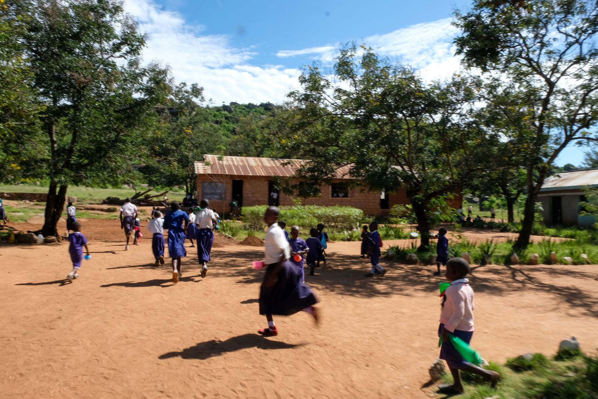 Tanzanian children run away from camera toward a building on a dirt road