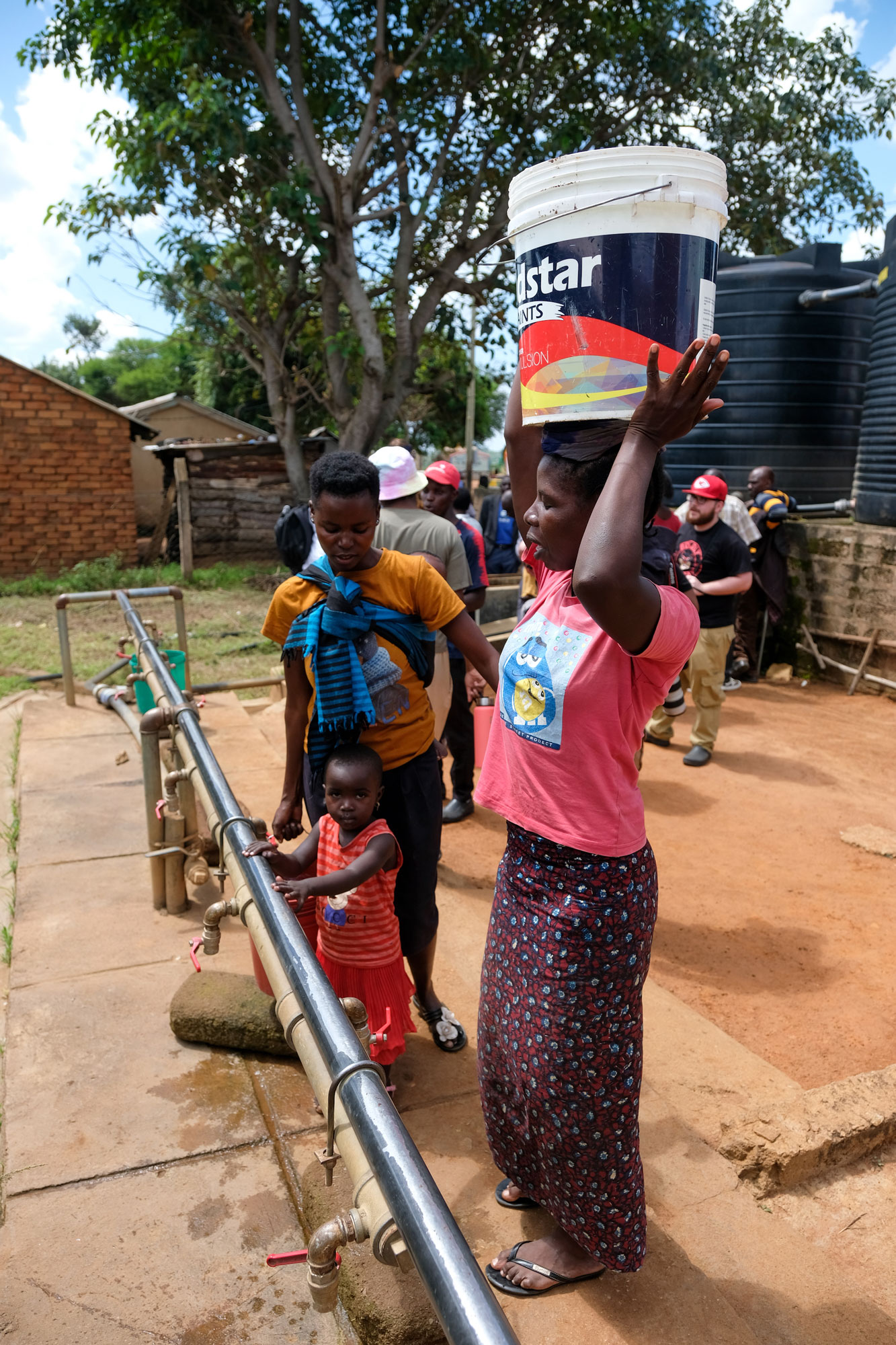 Tanzanian woman balances a large bucket of water on head
