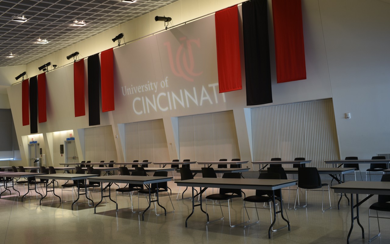 Long tables and chairs set up in rows along the side of a large meeting room..