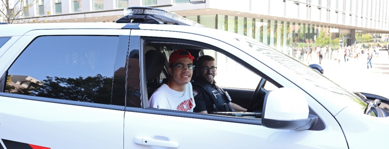 A UC student and a UCPD officer sit in a cruiser.