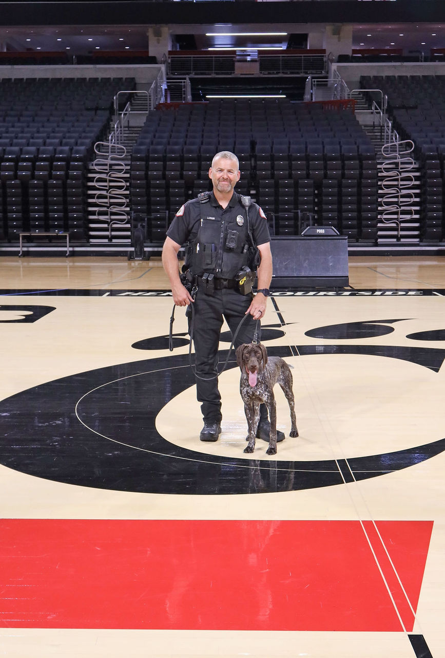 Officer Steve Lawson poses with K-9 Remi standing in the C-Paw on the court in Fifth Third Arena.