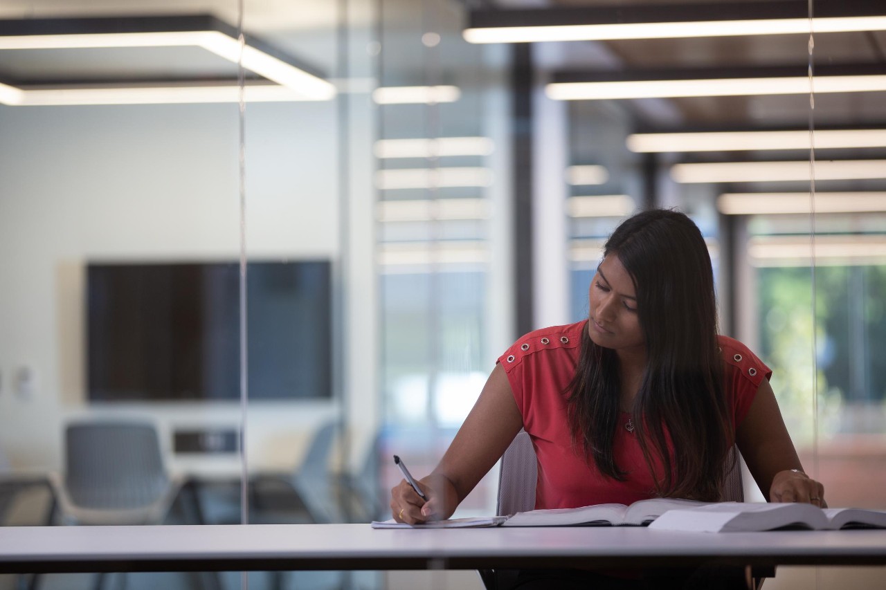 A woman sits at a table writing a letter of interest to a future employer