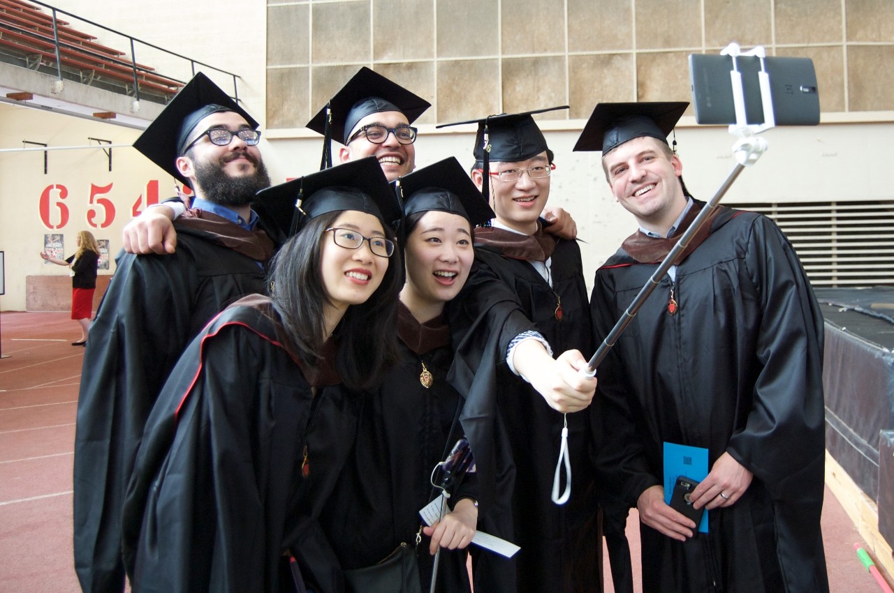 A group of UC students pose for a photo in their graduation cap and gown.