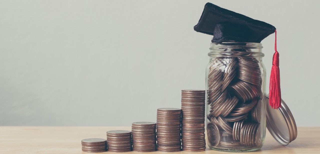 Stacks of coins and coins in a jar with a graduation cap on it - indicating saving money for college