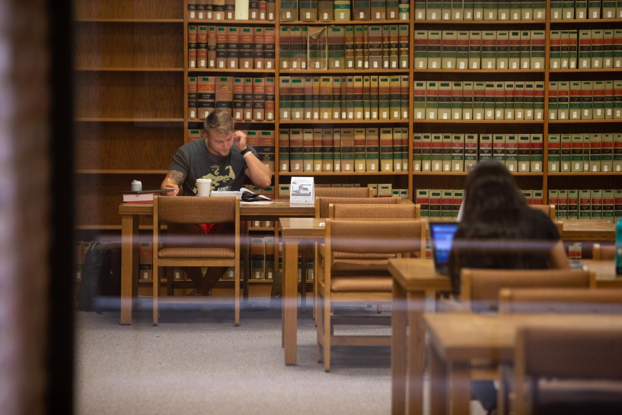 A male UC student studies a book while sitting at a table in a library.