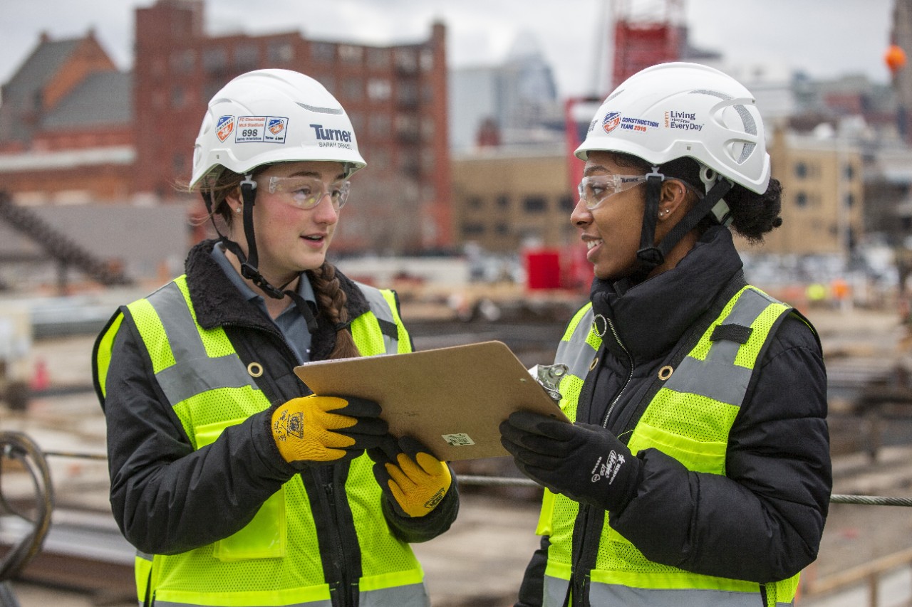 Two co-op students talk while holding a clipboard on a job site