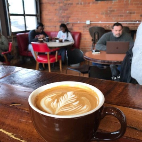 A photo of a cup of coffee with people in the background at 86 Coffee Bar in CCM.
