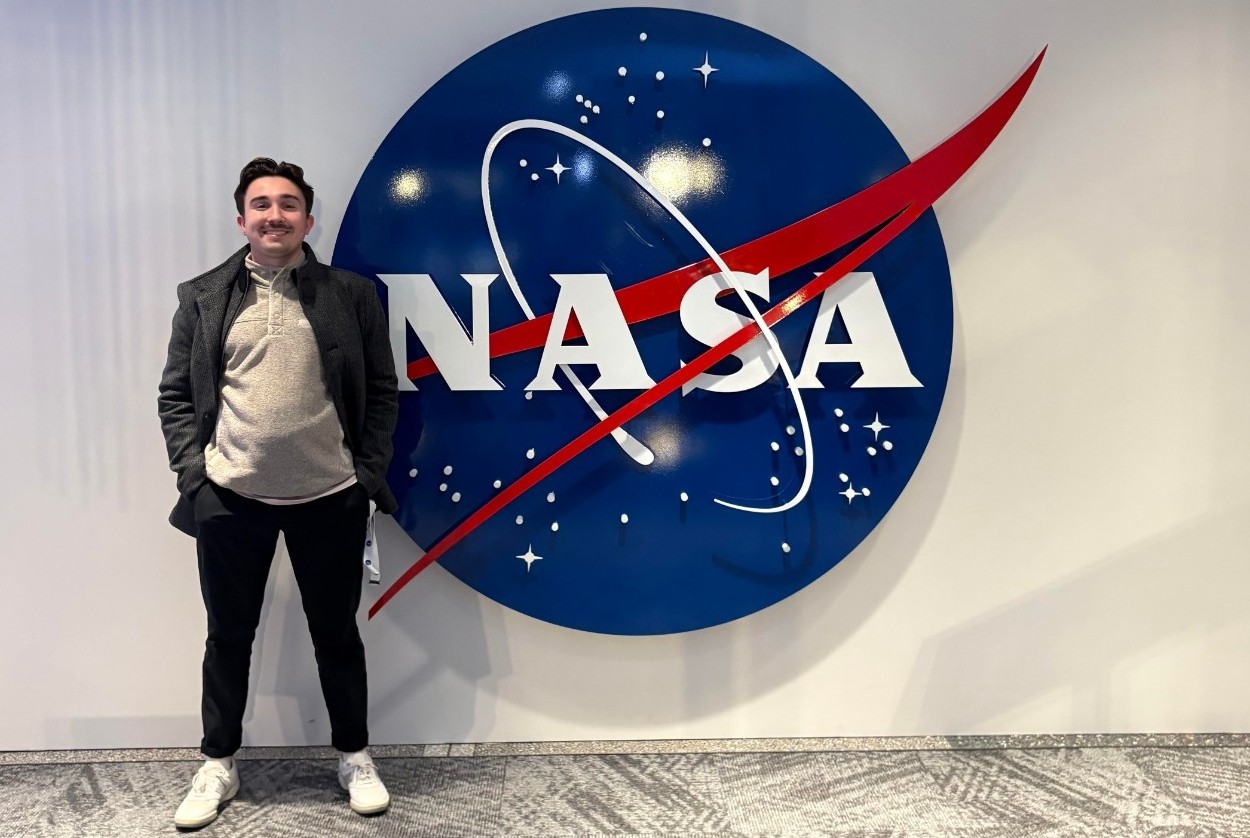 UC co-op student stands in front of NASA logo