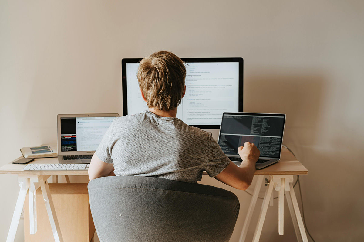 College student sitting at desk exploring micro-credentials on three computer screens, photographed from behind