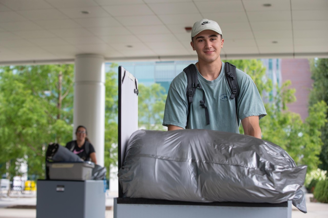 Should you go far away for college? This student smiles as he pushes a cart of belongings as he moves onto UC's campus.