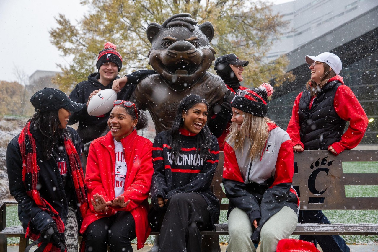 UC student laugh together on campus next to the Bearcat statue.