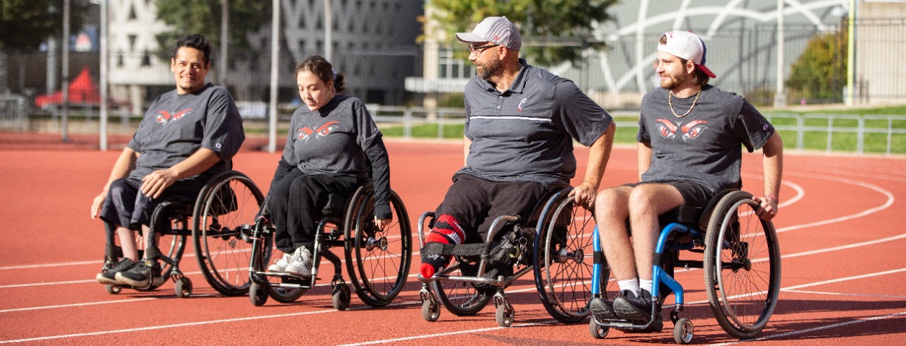 4 UC Athletes in wheelchairs on the UC Track wearing UC t-shirts