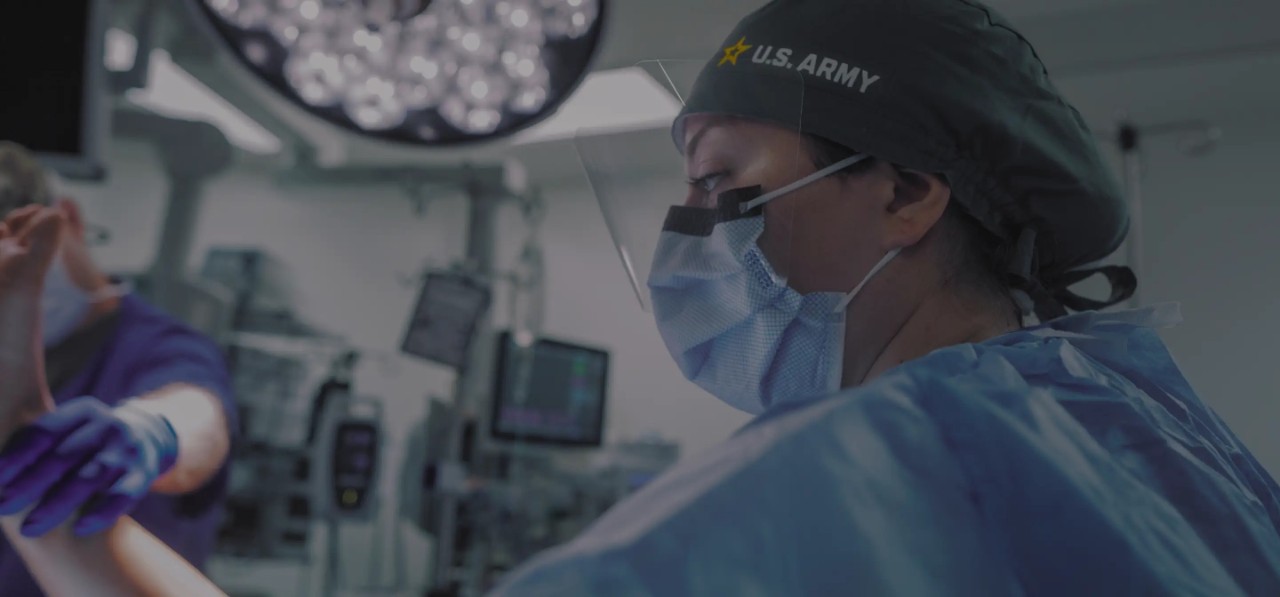 An army nurse wearing protective face mask and gown while working on a patient. 
