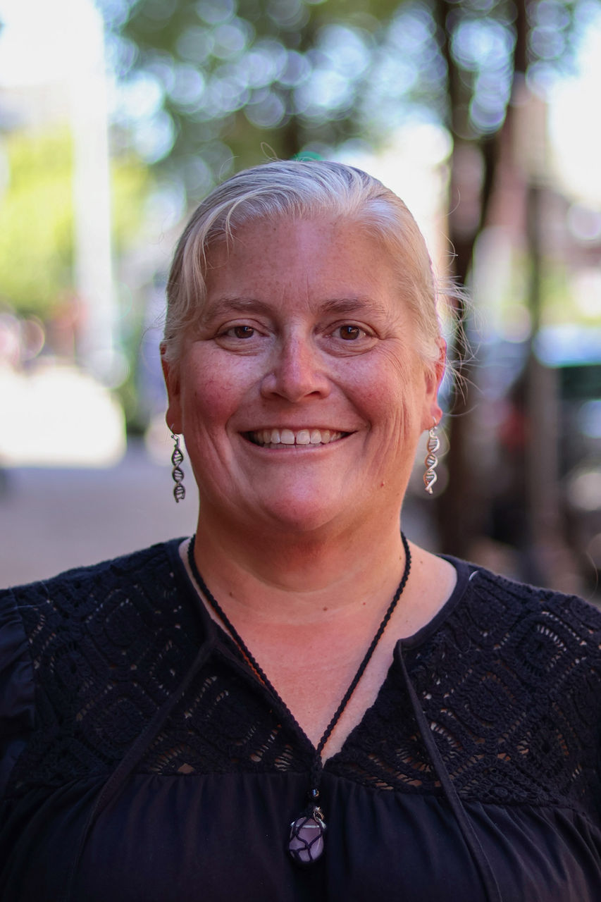 Photograph of Amy Blankenship outside of the CAPS building. She is smiling and wearing a black top.