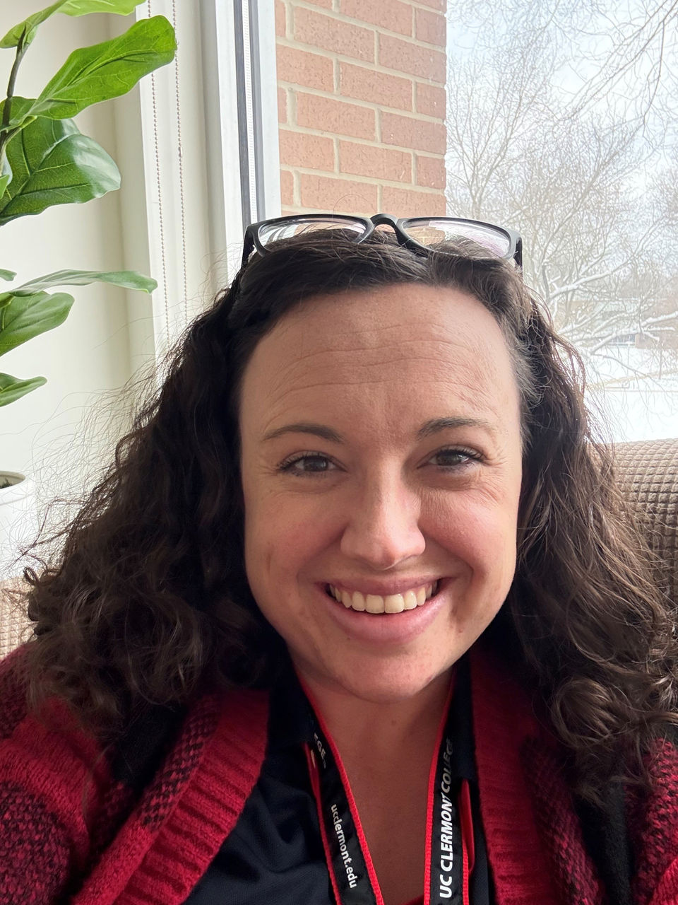 Photograph of Angela Hinrichsen smiling in her office at Clermont. She is wearing glasses a top her head like a hair band and a comfortable red sweater. 