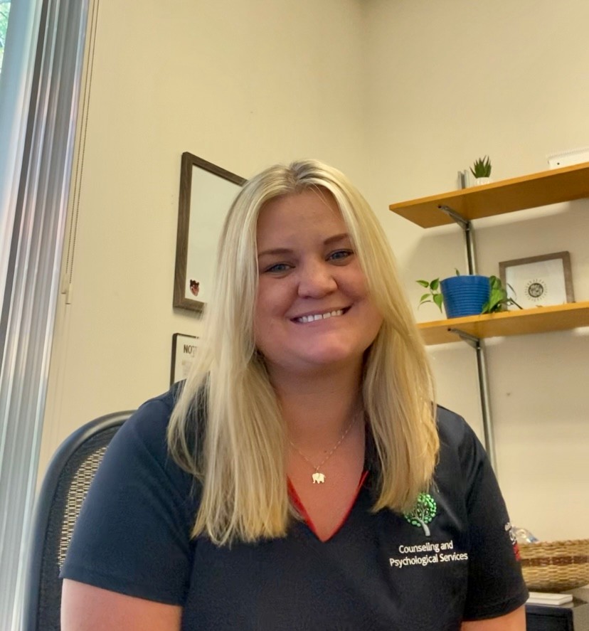 Photograph of Caity Cavanaugh smiling in her office. She is wearing a CAPS polo. 