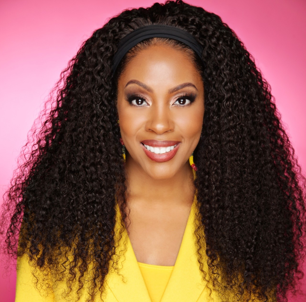Photograph of Calisha Brooks smiling in professional headshot. She is wearing a yellow suit jacket and standing in front of a pink background. 