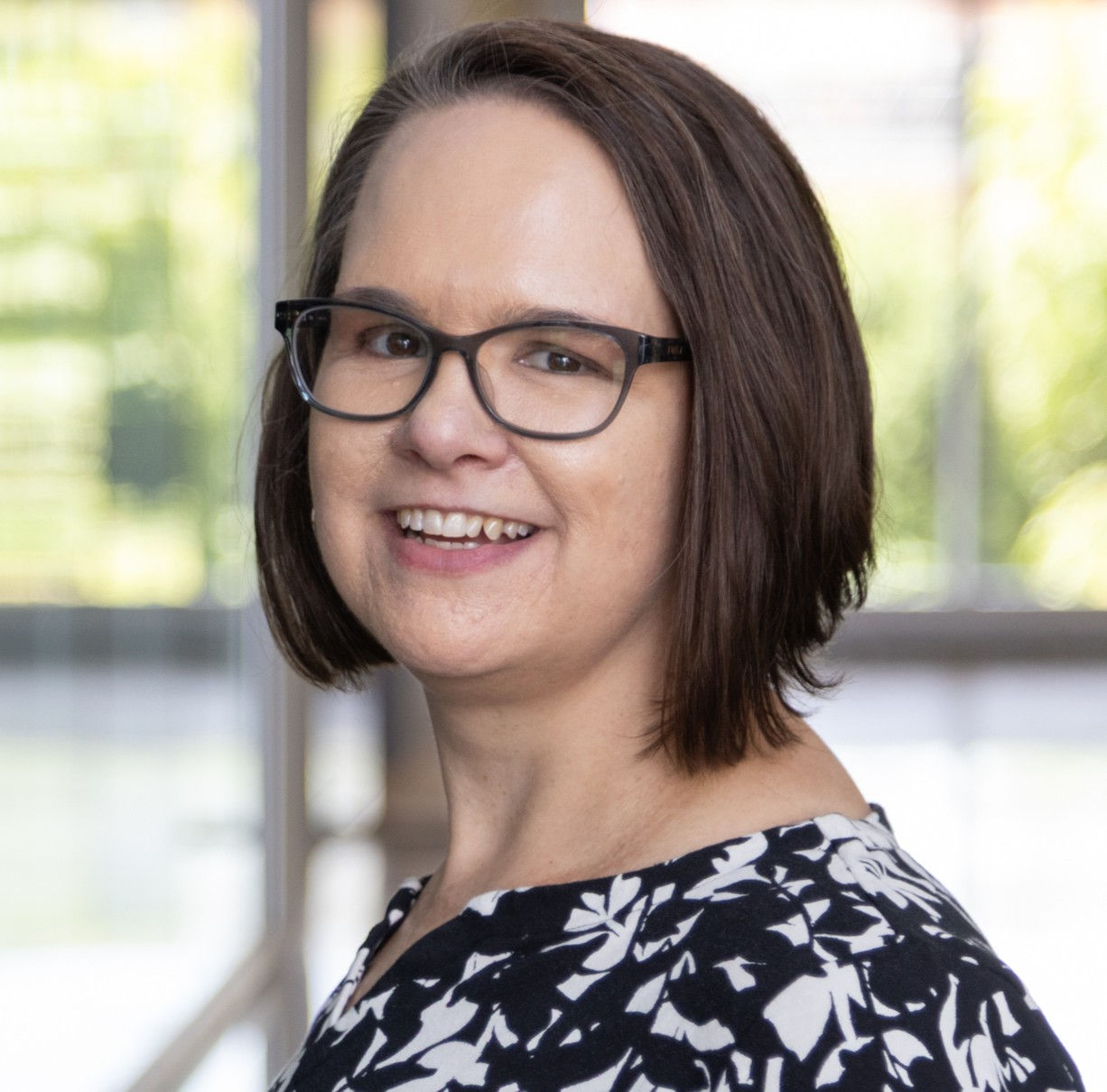 Photograph of Christy Wolfram smiling in CAHS building. She is wearing glasses and a black and white print top. 