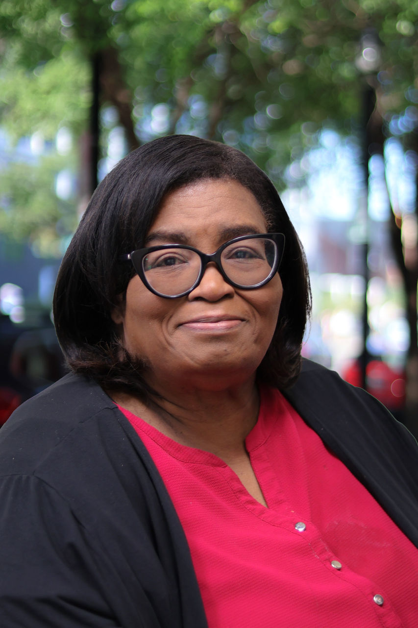 Photograph of Kim smiling outside of the CAPS building. She is wearing black and red. 