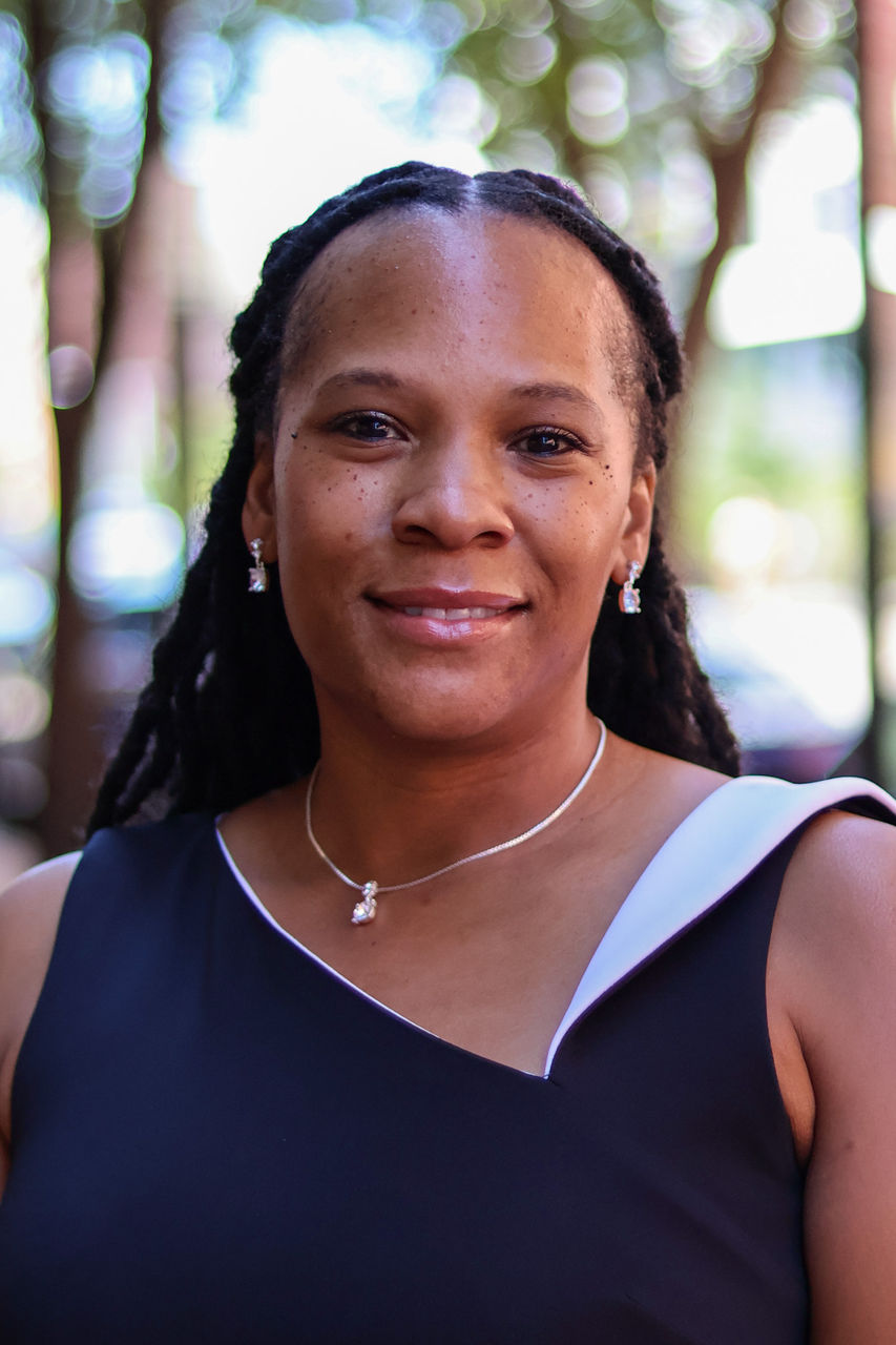 Photograph of LaSondra Wayne smiling outside of CAPS building. She is wearing a black and white top. 