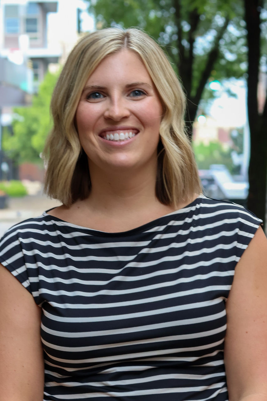Photograph of Madeleine Muller smiling outside of CAPS building. She is wearing a black and white striped top.