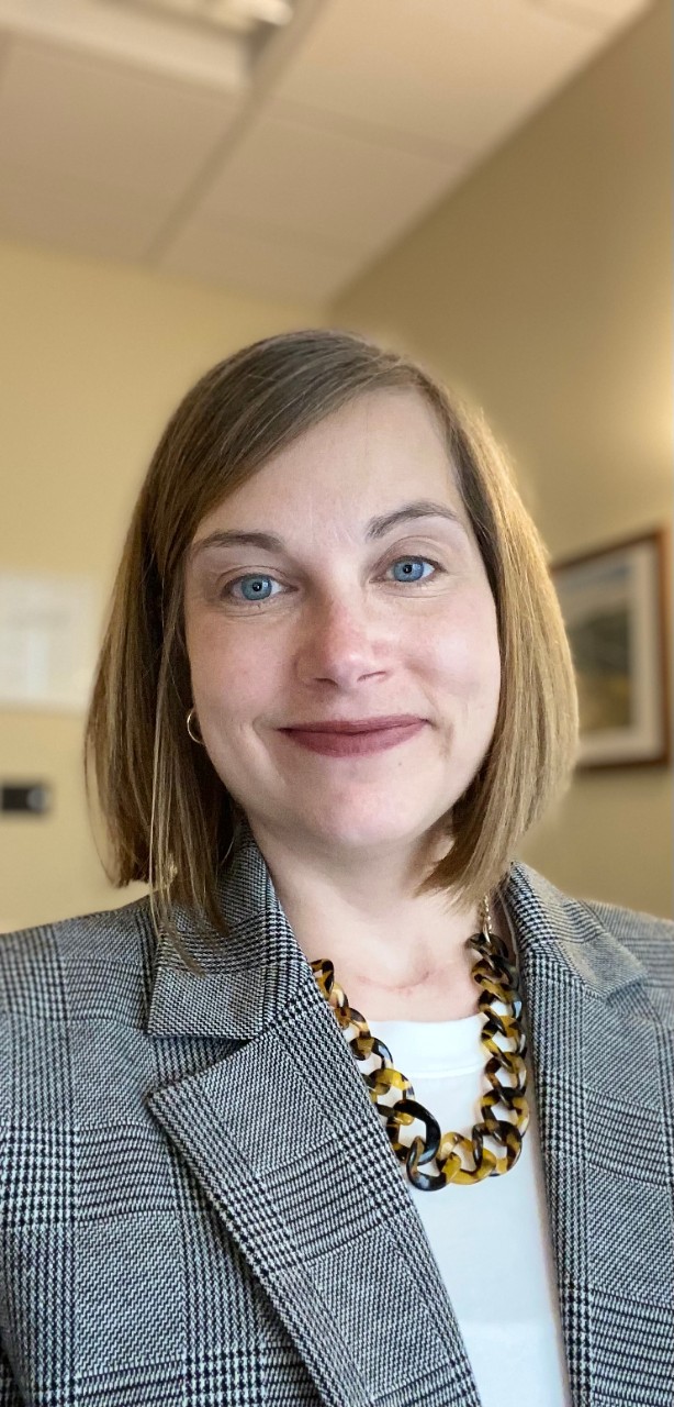 Photograph of Monica Gray in her office. She is smiling and wearing a gray jacket and patterned necklace.