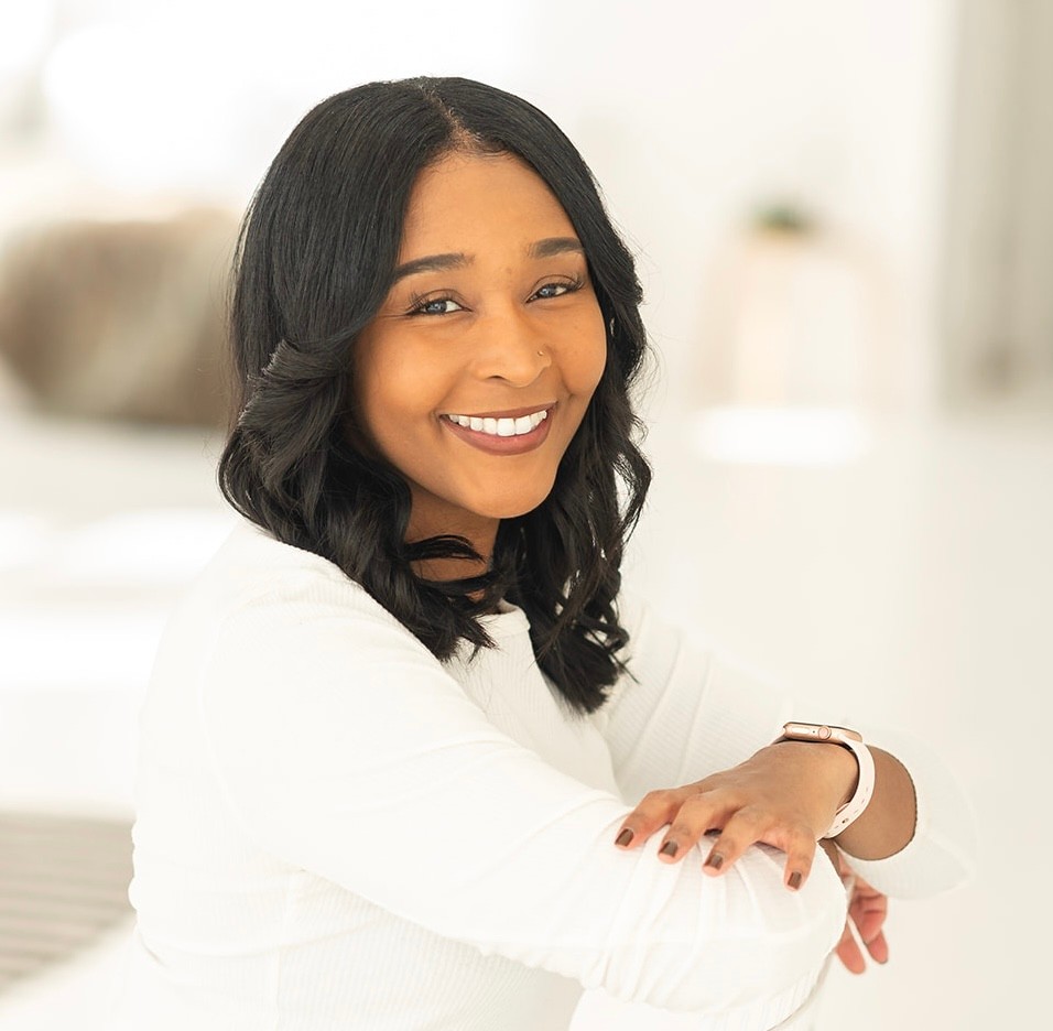 Photograph of Nyla Morgan smiling in a professional headshot. She is wearing a white outfit and is sitting outside. 