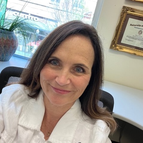 Photograph of Tara Scarborough in her office and smiling. She is wearing a white top.