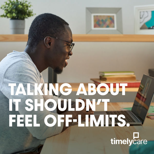 Photograph of a black male student sitting at a table and engaging with therapy on their laptap. The words "Talking about it shouldn't feel off-limits" is on the photograph in white lettering. 