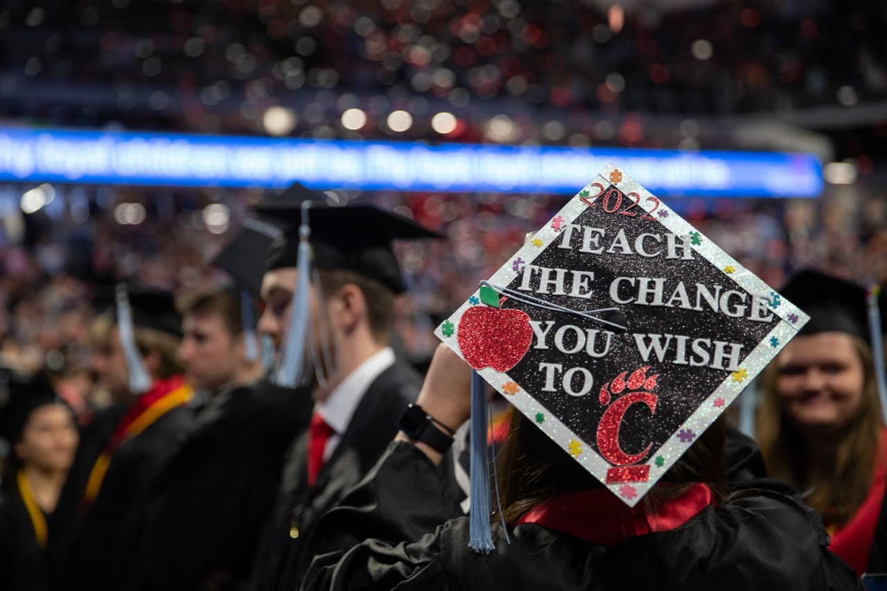 A birds eye view of a graduation cap reading "Teach the Change You Wish to C" and an apple. The C is represented by a C-paw.
