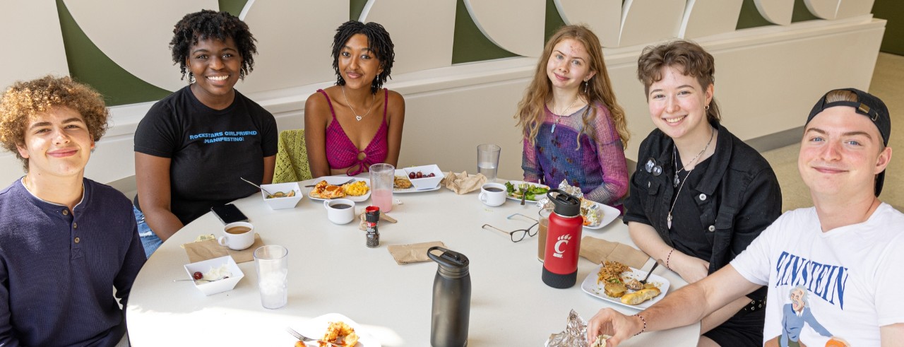 A food worker serves a plate to a student while others smile while waiting in line.