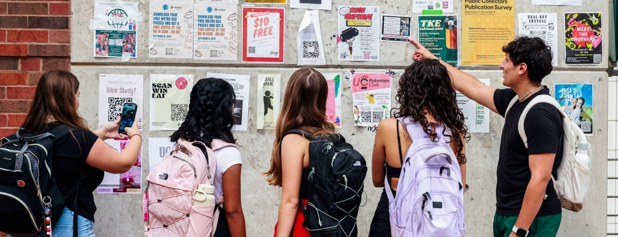 Students looking at a bulletin board full of flyers.