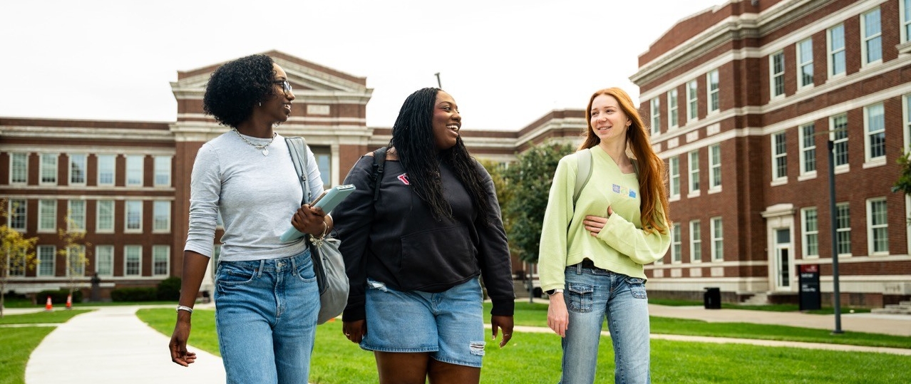 3 students walking on a path smiling on campus