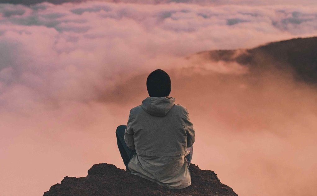 Person sitting on a cliff over a sea of clouds